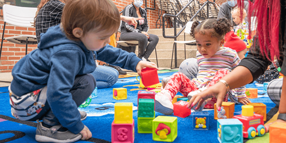 Two toddlers playing with colorful blocks on a blue mat.