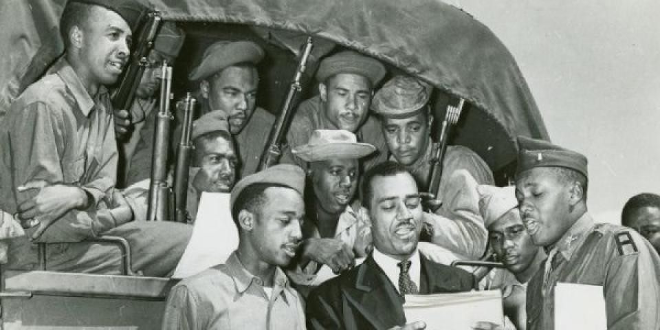 African American soldiers of the 372nd sitting in a truck with their guns and looking at papers 