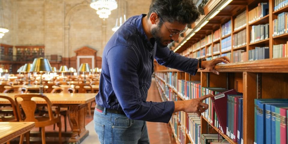 A researcher pulls a book from a shelf in the Rose Main Reading Room. 