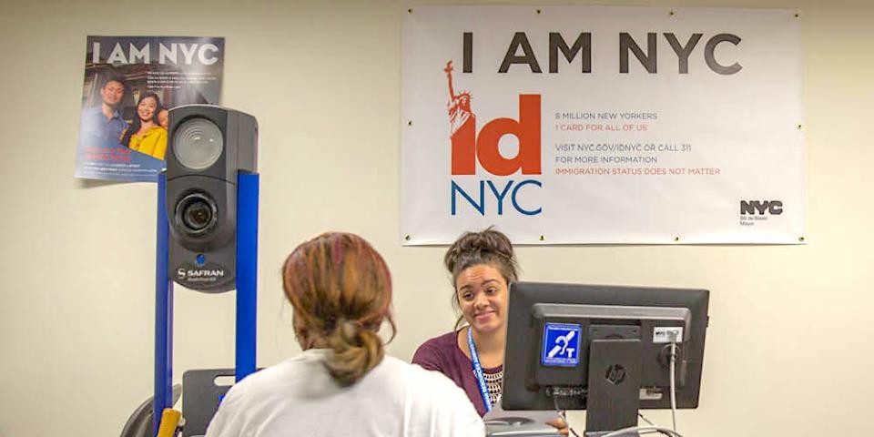 A person applies for an idNYC card at a desk with idNYC signs behind it.