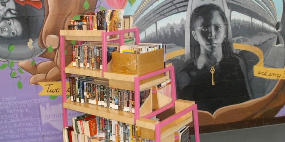 Photo of a book cart in front of a wall with a colorful, photorealistic mural.