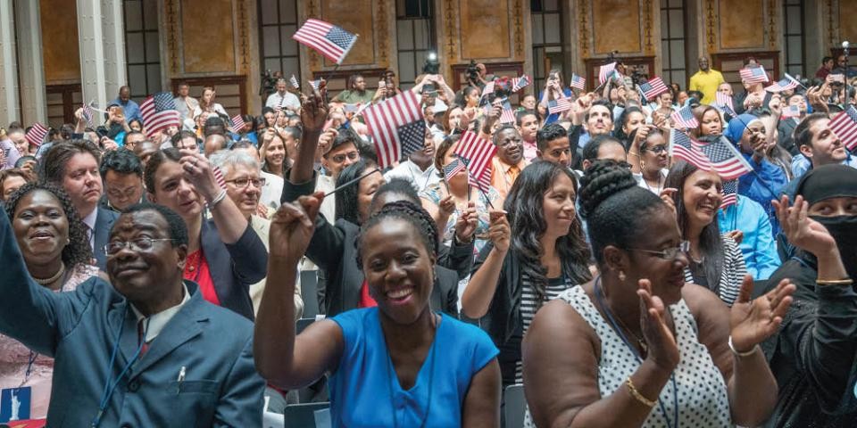A room full of people smile and wave American flags during a U.S. naturalization ceremony. 