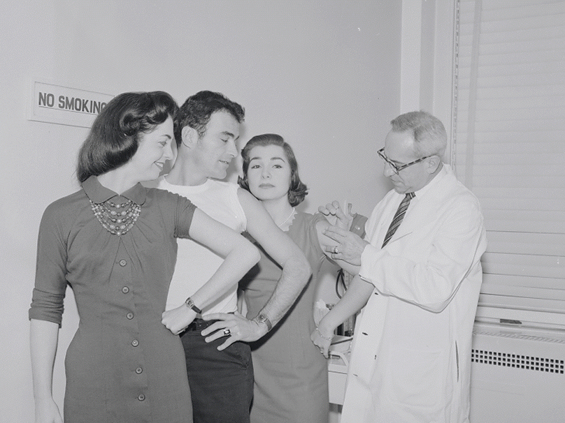 Publicity shot of performers receiving a vacination. Photo by Friedman-Abeles 
