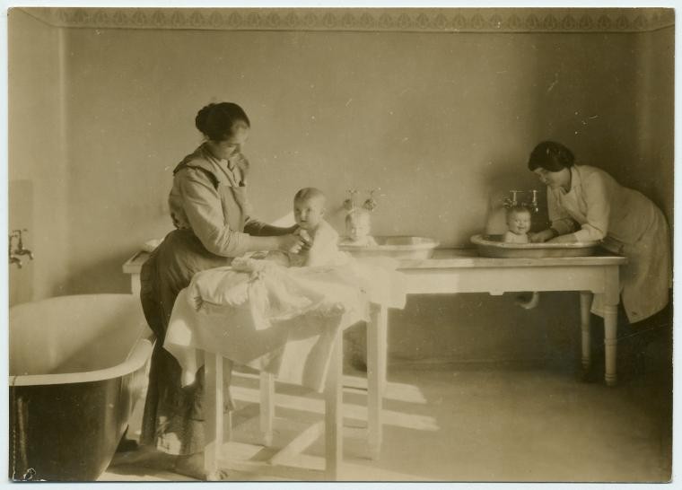 two nurses, each holding a baby in a tabletop bath