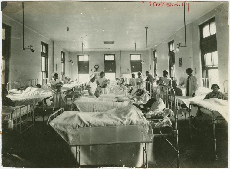 large room with metal beds filled with patients as nurses and doctors attend them