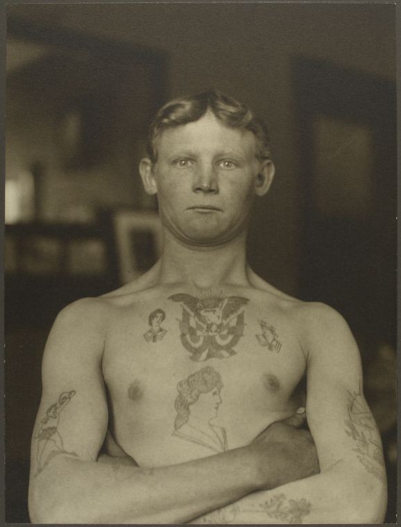 shirtless young man with arms crossed and tattoos on his chest and arms
