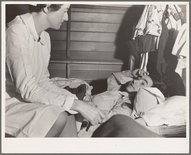 nurse sitting speaking to a patient lying in bed