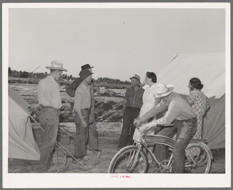 woman nurse speaking to migratory farm workers near a tent