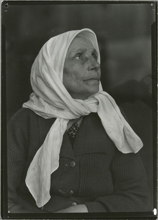 an older woman with a white shawl around her head looks skyward