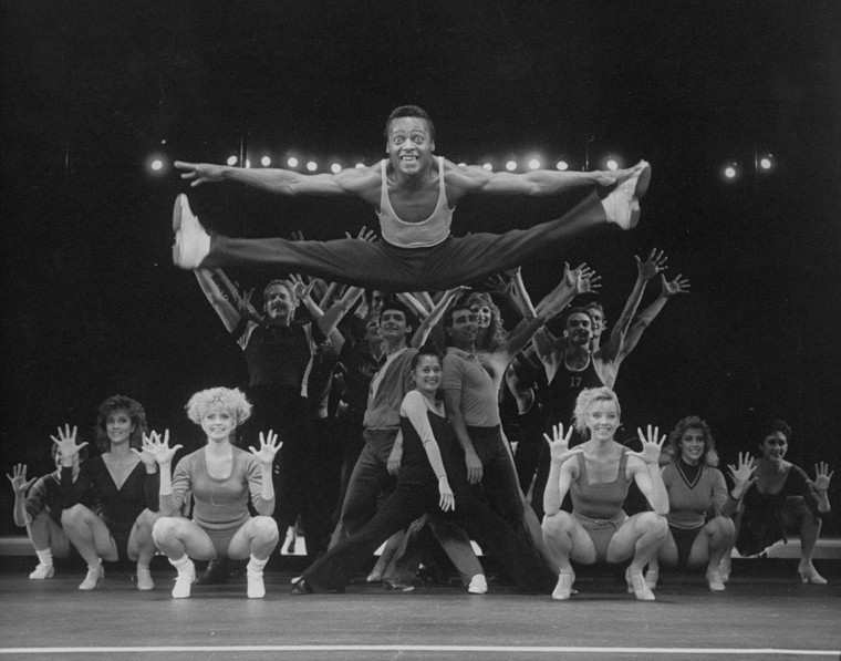 man in mid-air split with dancers behind him