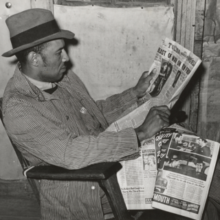 A male sitting in profile reading a newspaper