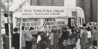 Black and white photograph of a line of children outside a bus filled with books.