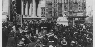 Black and white photograph of a crowd on the steps of the Schwarzman Building. A sign of a cartoon soldier reads: Books wanted for our men in camp and over there. 