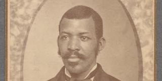 close portrait of a black man in a black colored suit, a white shirt, and a dark colored bow tie