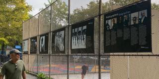 Brown banners with black and white and color photos hanging on a fence in a park.