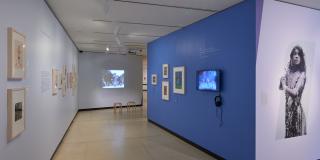 Photograph of a corridor in exhibition with frames on the side walls and a projection at the end. 