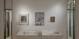 White wall with three framed pieces of artwork and two white hanging cases of flat archival material