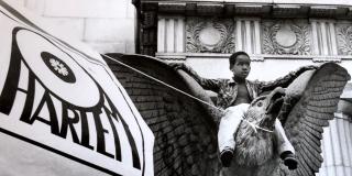 Black and white photograph of young Black boy sitting on top of eagle statue.