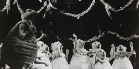 A black and white photo of several mice kneeling in front of a Christmas tree. A larger mouse is standing to the left.