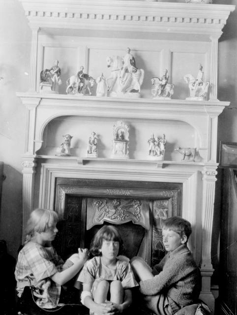 black and white photograph of three young children in front of a mantle and fireplace