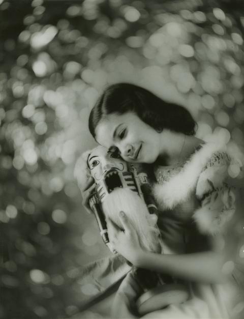 A black and white photo of a girl in a dress hugging a nutcracker in front of a glittering background.