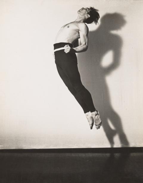 Black and white photo of José Limón mid-jump with his back arched, chest raised, and head thrown back, casting a shadow on the wall behind him.